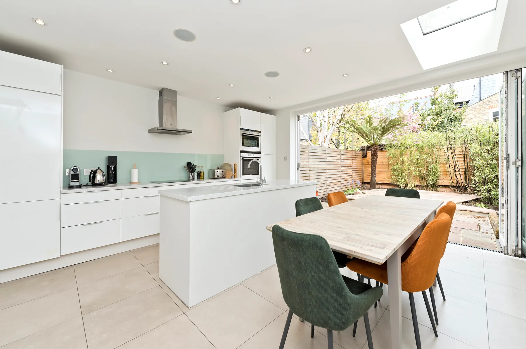 A bright modern kitchen and dining area opens onto a fenced garden.