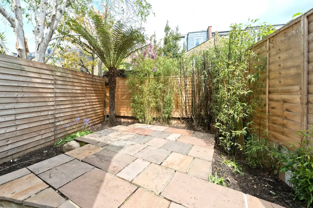 A paved outdoor patio is bordered by wooden fencing and green plants.