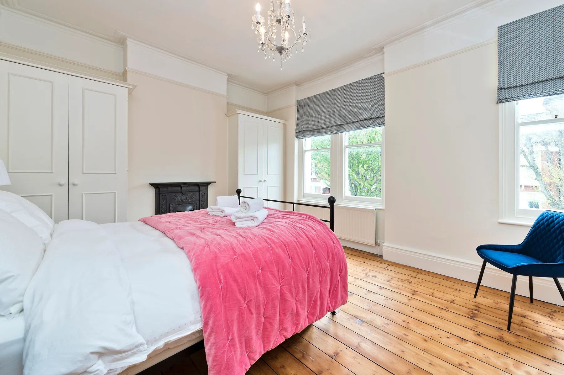 A bedroom with a bed covered by a pink blanket beside bright windows.