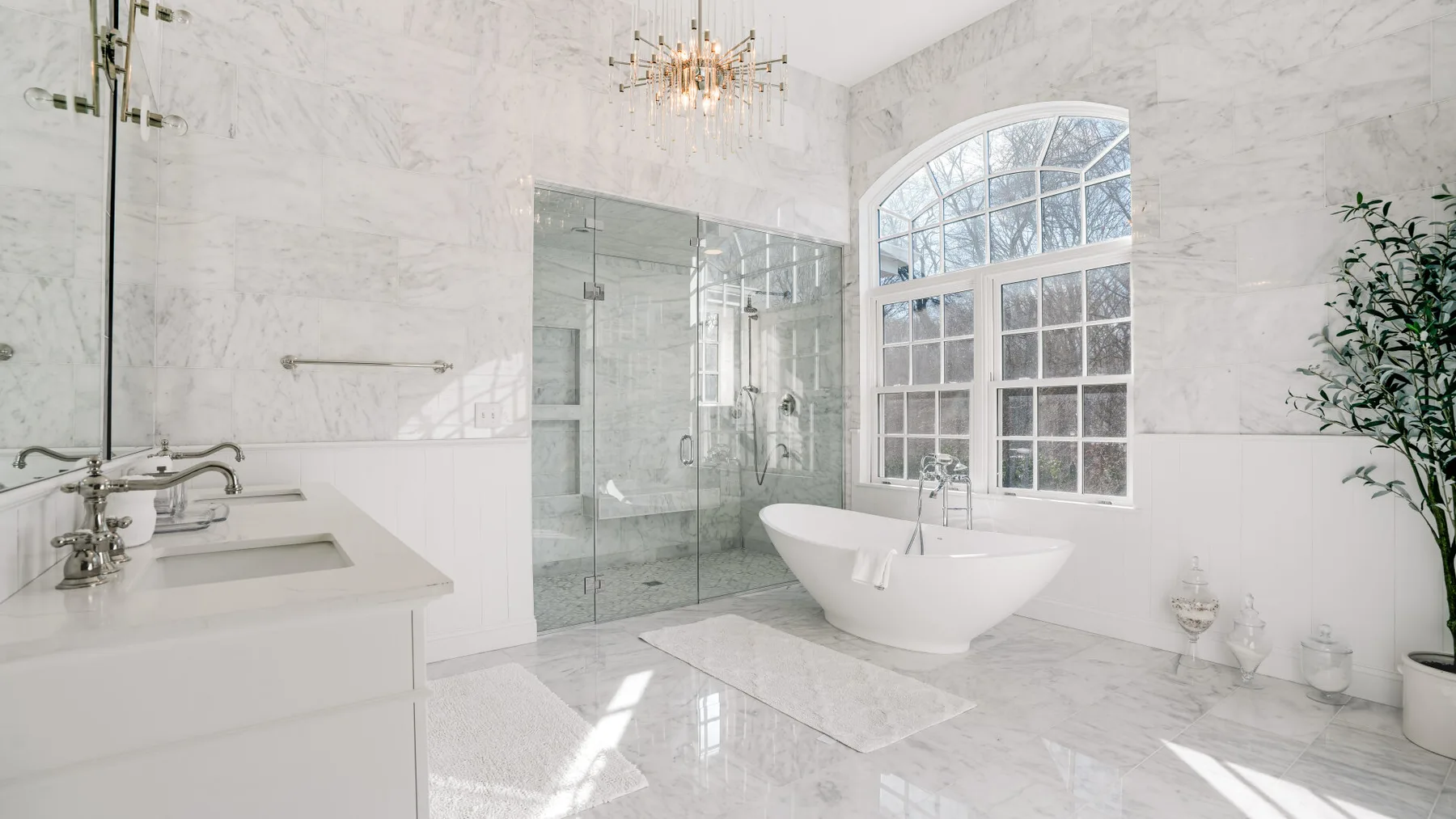 Un baño luminoso con bañera exenta, ducha de vidrio y una gran ventana arqueada.