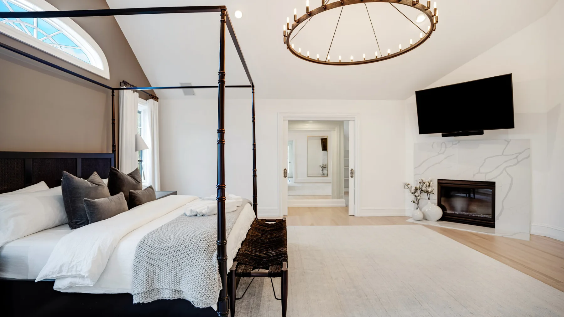 Un dormitorio luminoso con cama con dosel, chimenea y televisor en la pared.