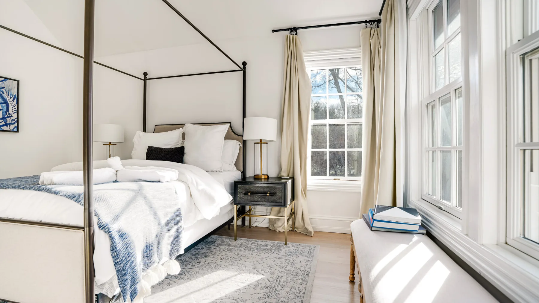 Un dormitorio luminoso con una cama con dosel y ventanas grandes.