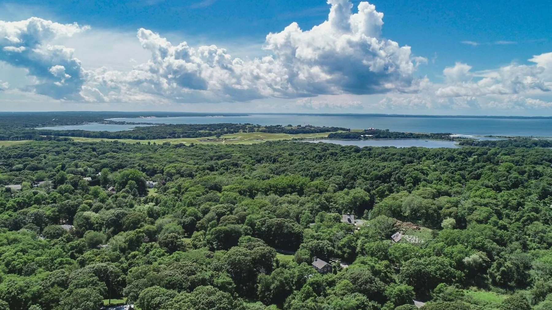 Un extenso paisaje verde se extiende hacia aguas lejanas bajo un cielo lleno de nubes.