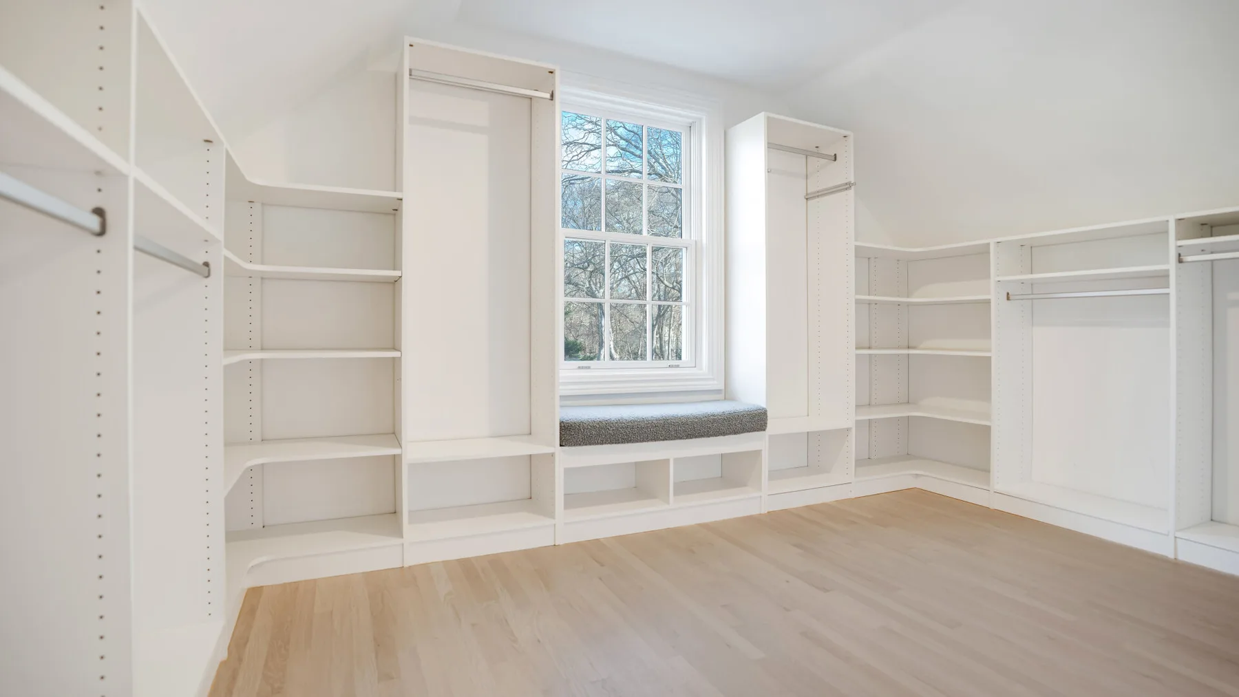 Un vestidor luminoso con estanterías empotradas blancas y una ventana.