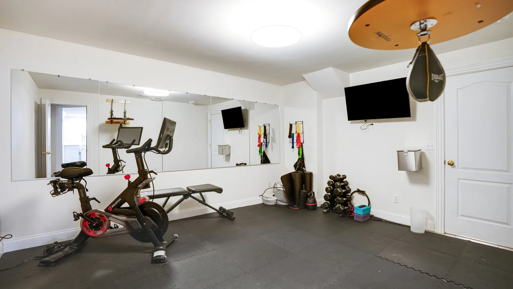 Un gimnasio en casa con equipo de ejercicio, pesas y un televisor en la pared.
