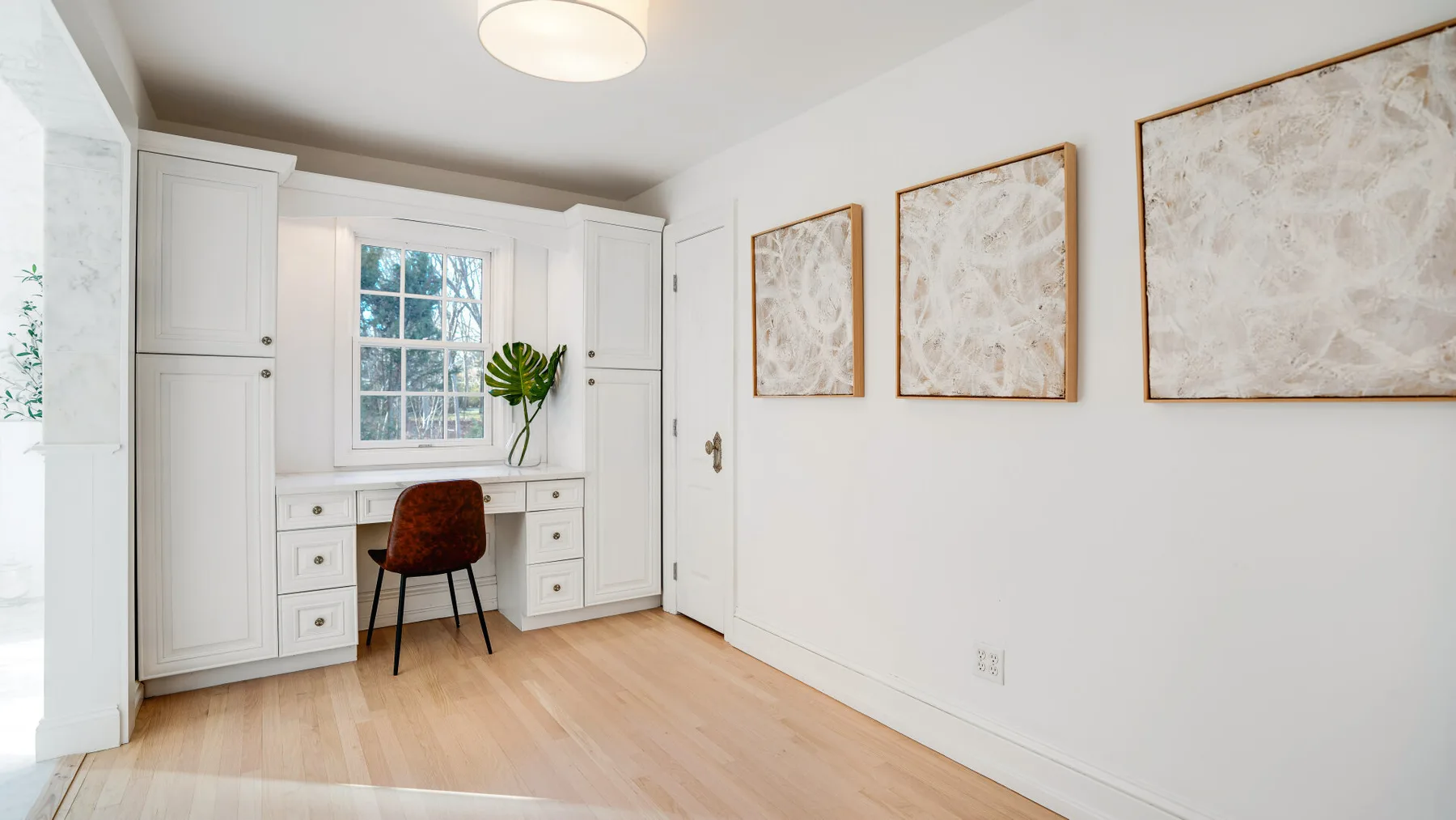 Una habitación luminosa con un escritorio empotrado bajo una ventana y cuadros enmarcados.