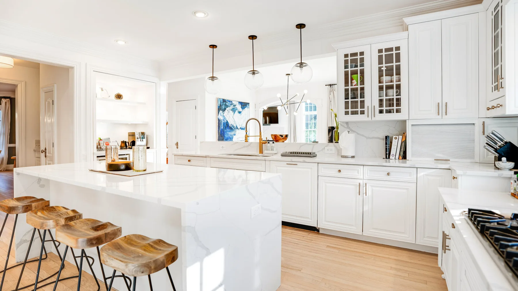 Una cocina blanca y luminosa con una isla grande y lámparas colgantes.