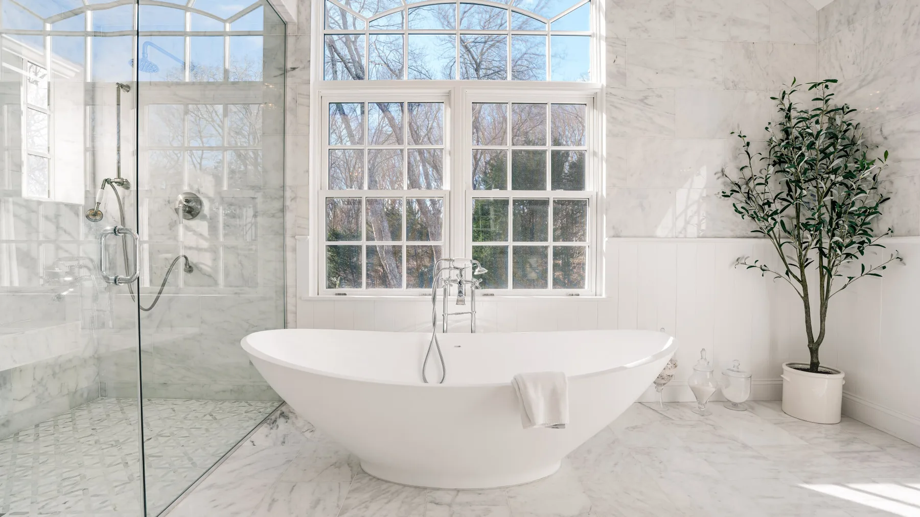 Un baño luminoso cuenta con una bañera exenta junto a una ducha de cristal y ventanas altas.