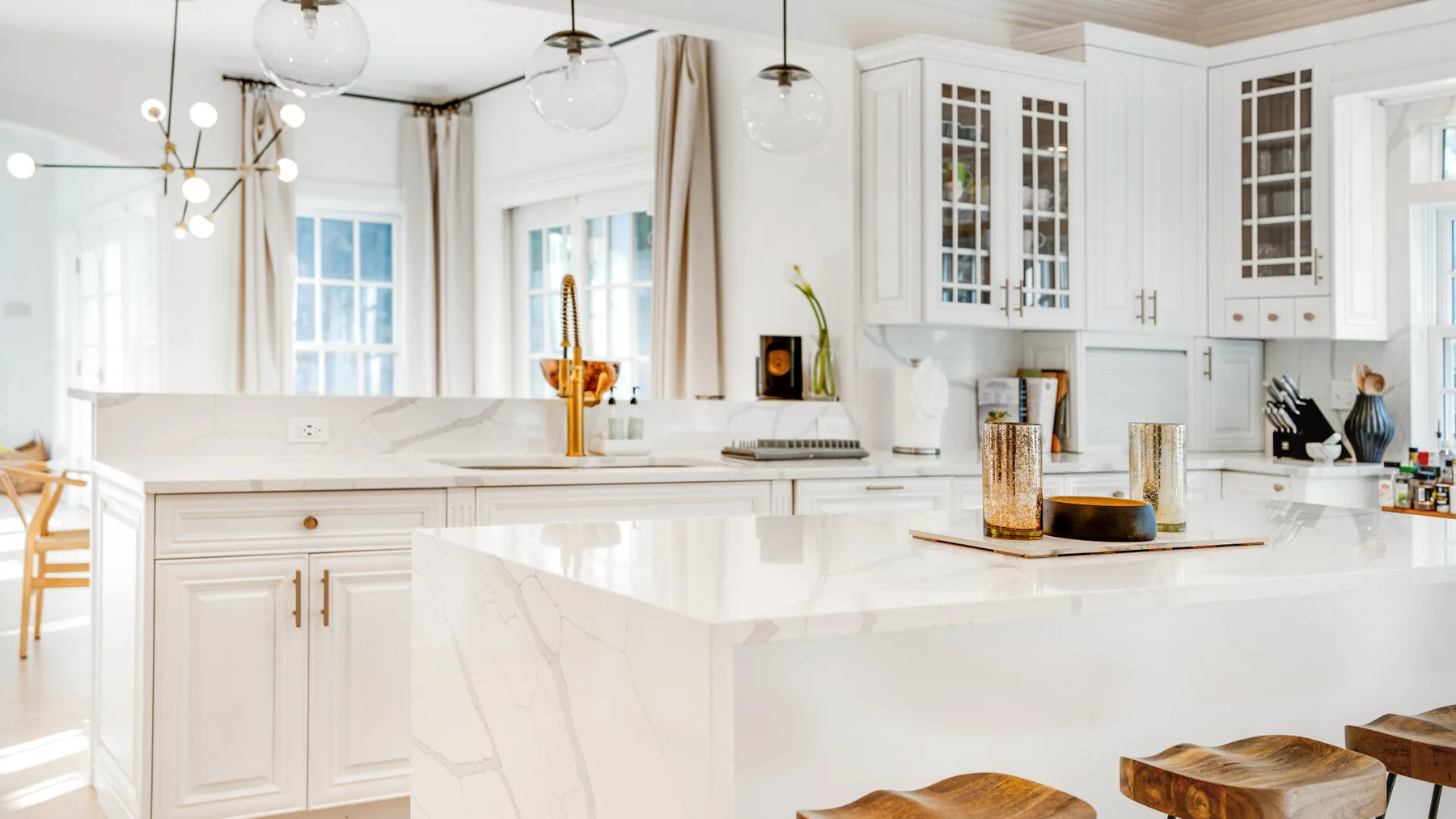 Una cocina blanca y luminosa tiene gabinetes con puertas de vidrio y una isla grande.