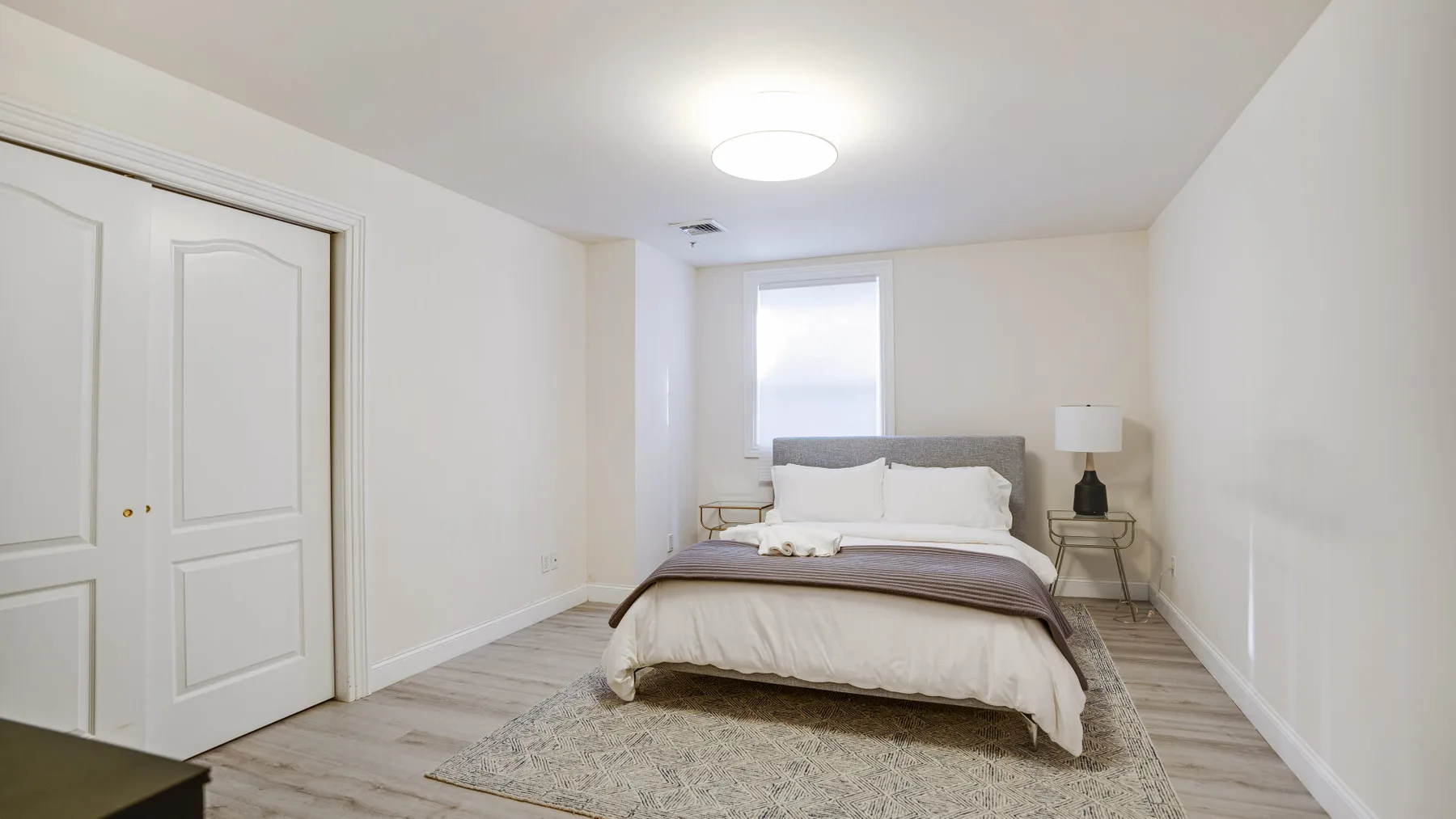 Un dormitorio con una cama, una ventana pequeña y una mesita de noche.