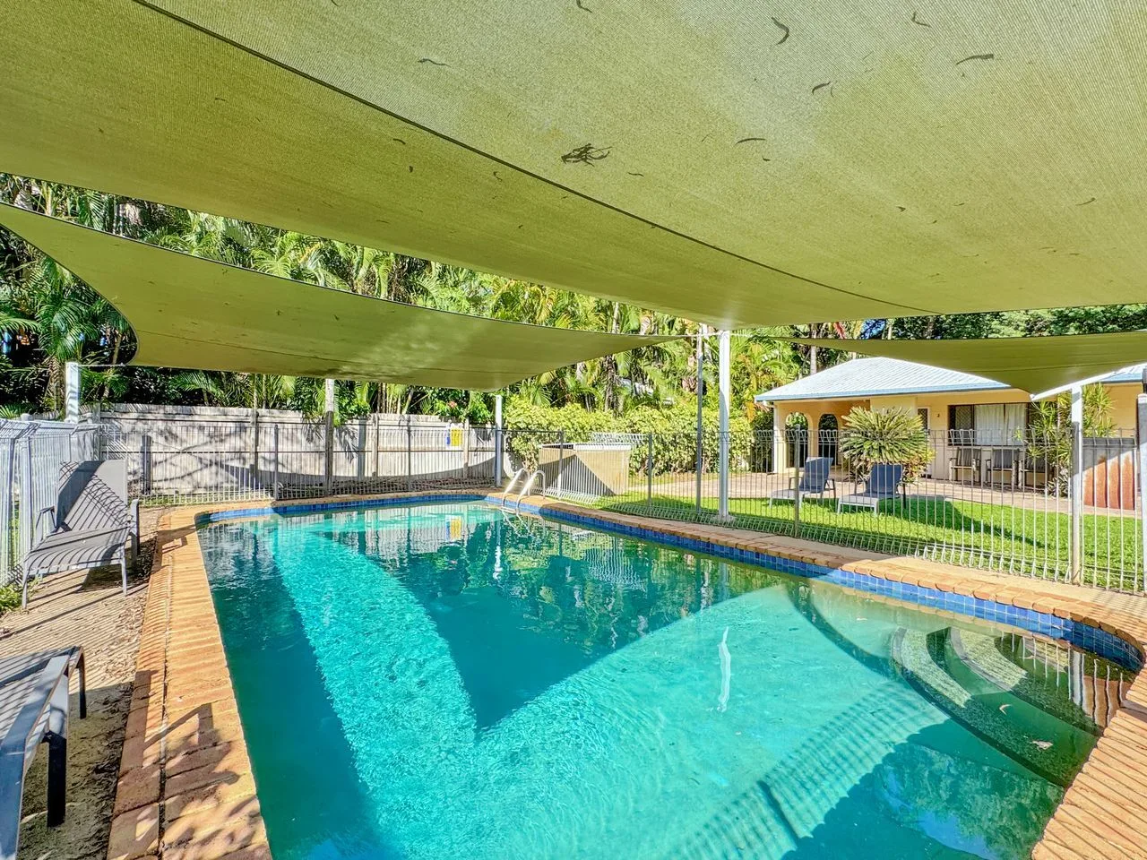 Una piscina al aire libre se encuentra bajo una amplia cubierta de sombra.