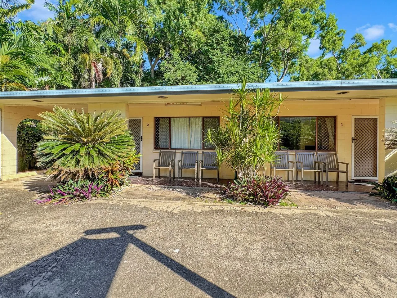Un edificio de una planta tiene un patio cubierto con asientos al aire libre y vegetación alrededor.