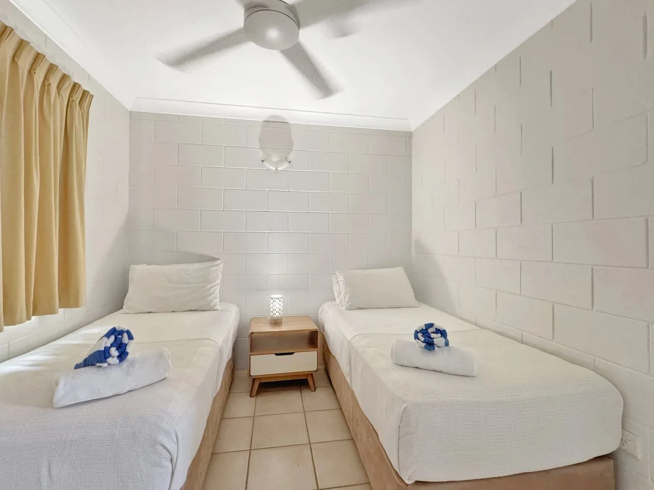 Un dormitorio con dos camas, ropa de cama blanca y una mesita de noche.