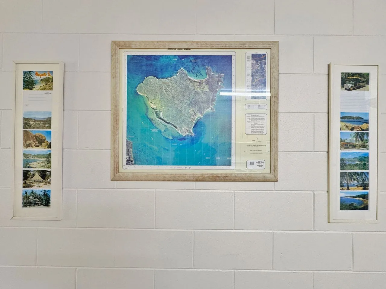 Exhibición en la pared con un mapa enmarcado de una isla entre dos collages de fotos estrechos.