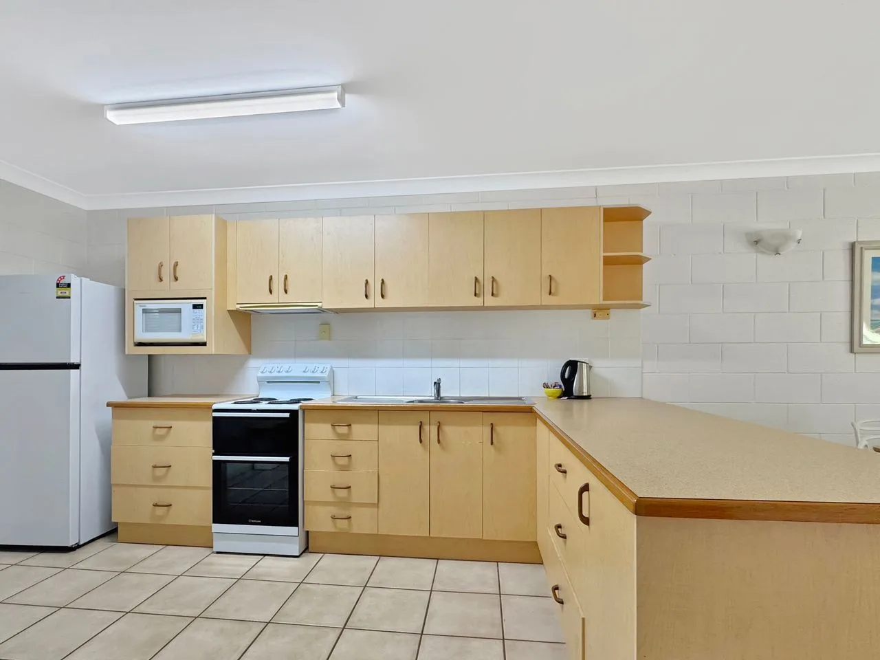 Cocina con gabinetes de madera clara, estufa y una encimera larga.