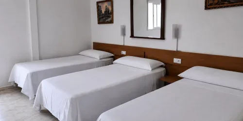 Habitación triple con tres camas individuales, un cabecero de madera, un espejo y ropa de cama blanca.