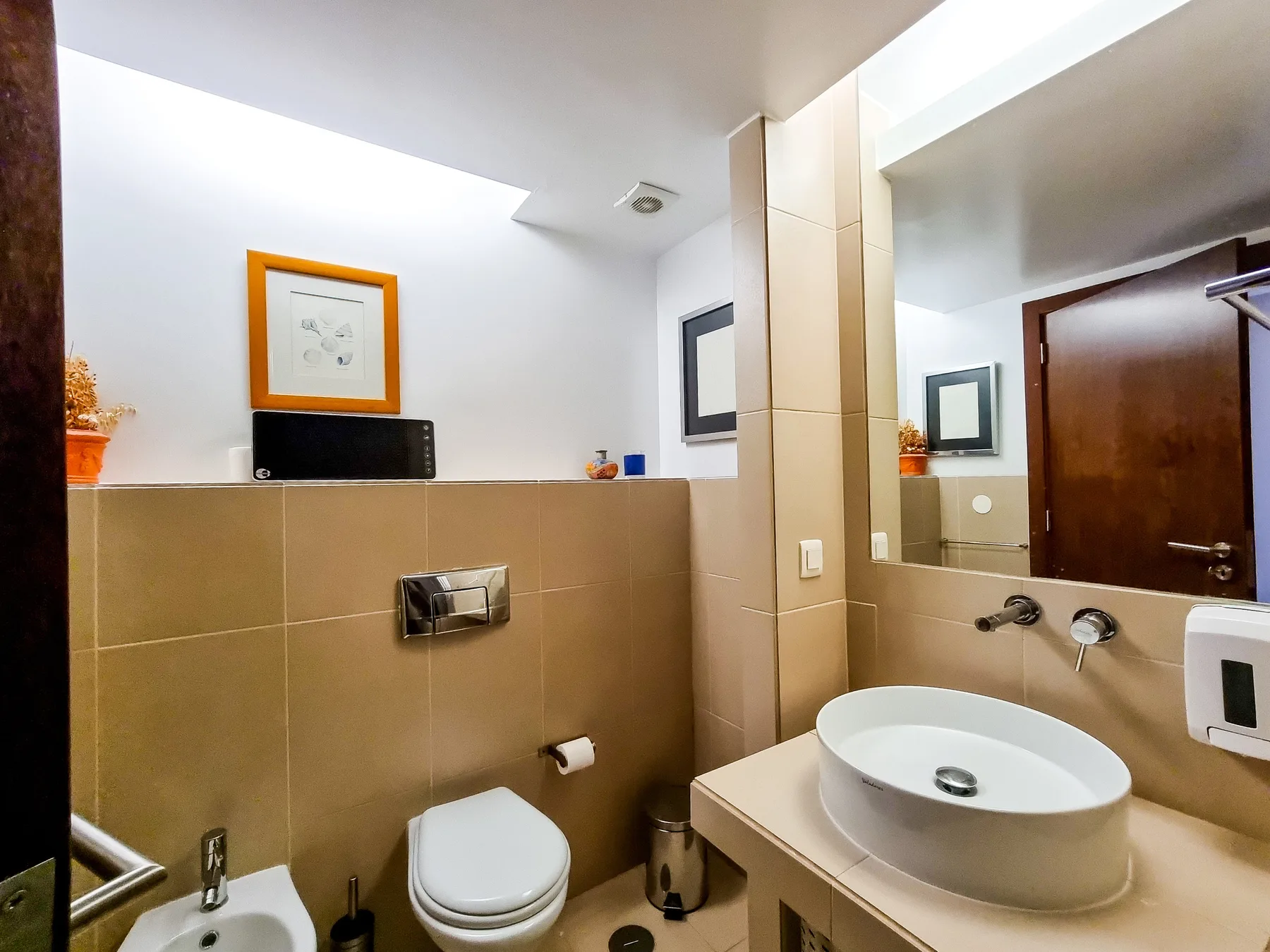 Un baño con inodoro, lavabo y paredes de azulejos color beige.