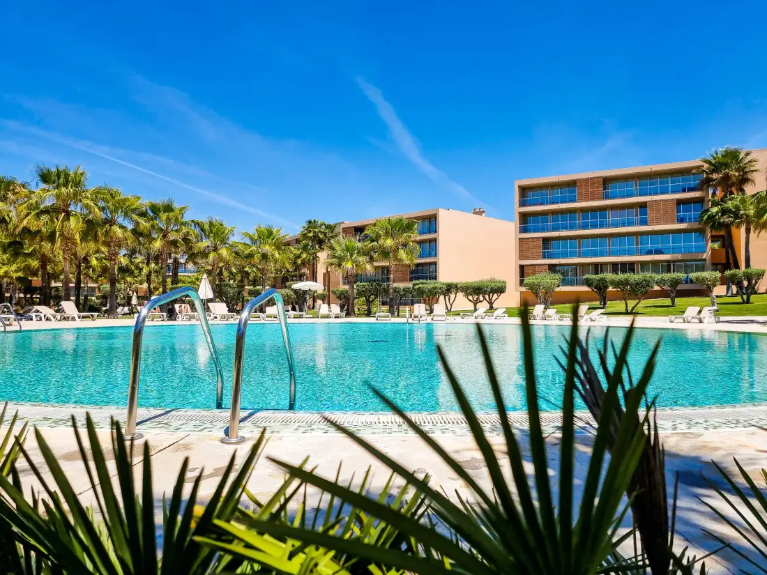 Una piscina al aire libre está frente a un edificio moderno y palmeras.