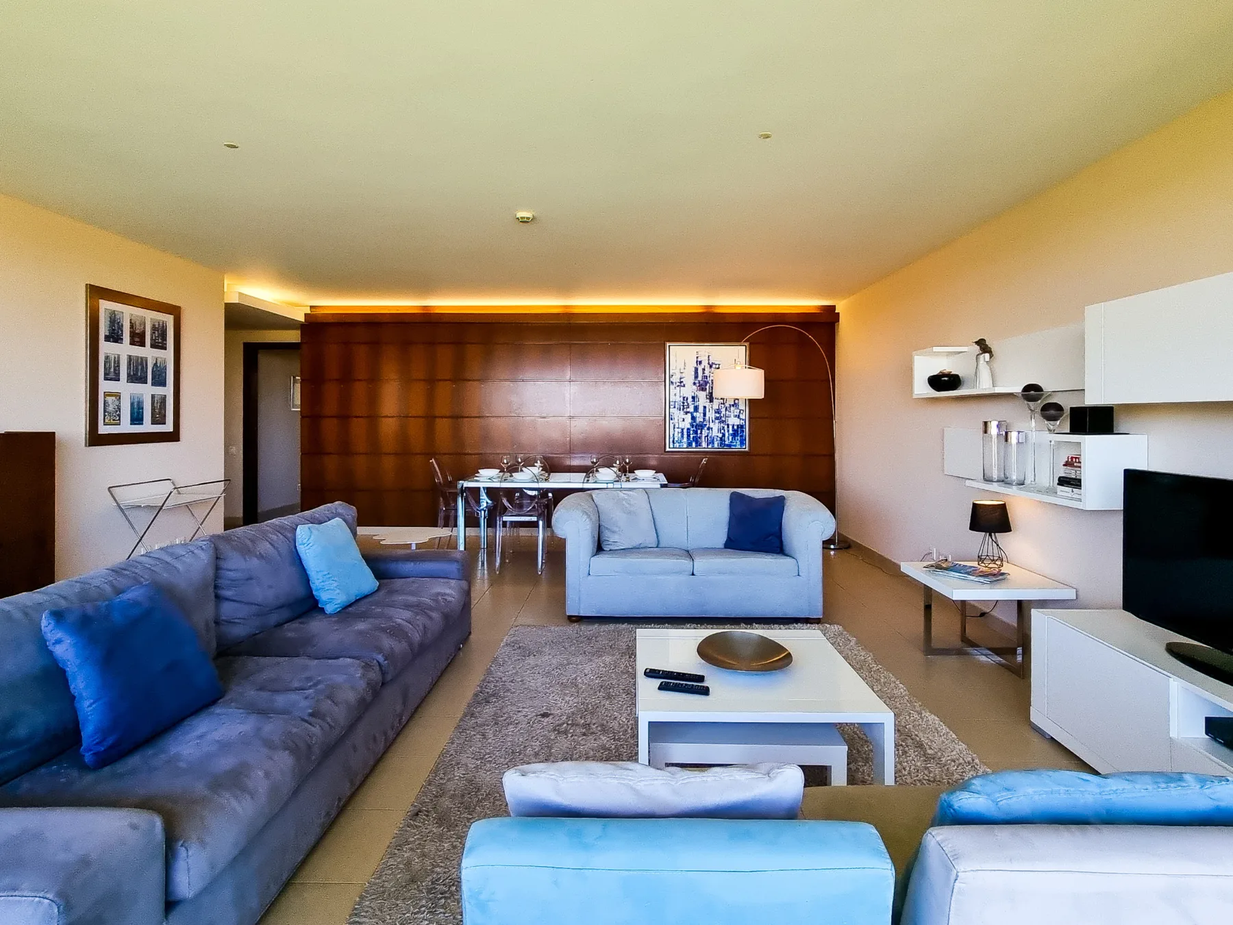 A living room with seating, a coffee table, and a dining area in the background.