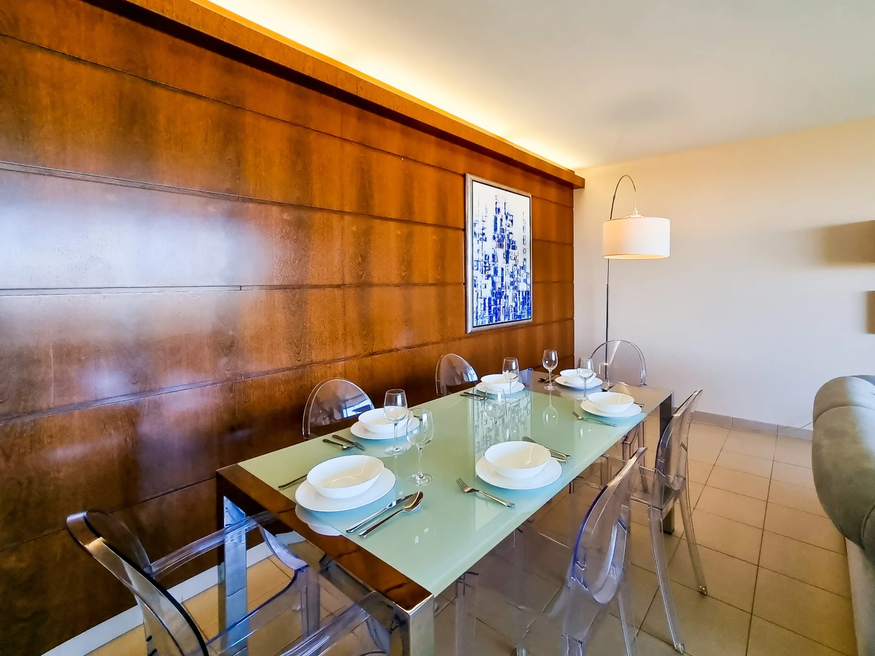 Comedor con una mesa de vidrio junto a una pared revestida de madera.