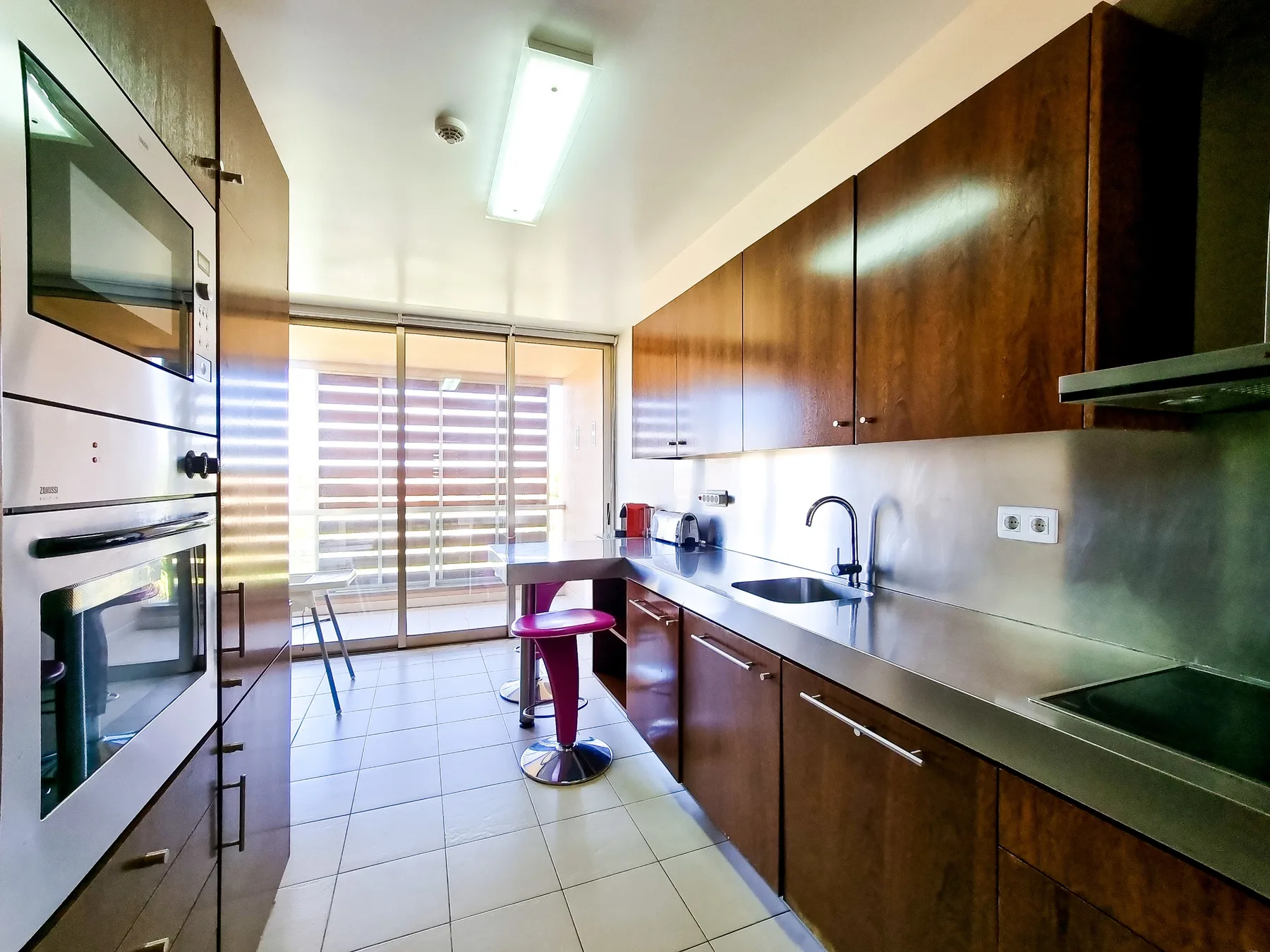 Una cocina con gabinetes de madera oscura, electrodomésticos de acero inoxidable y una mesa alta pequeña.