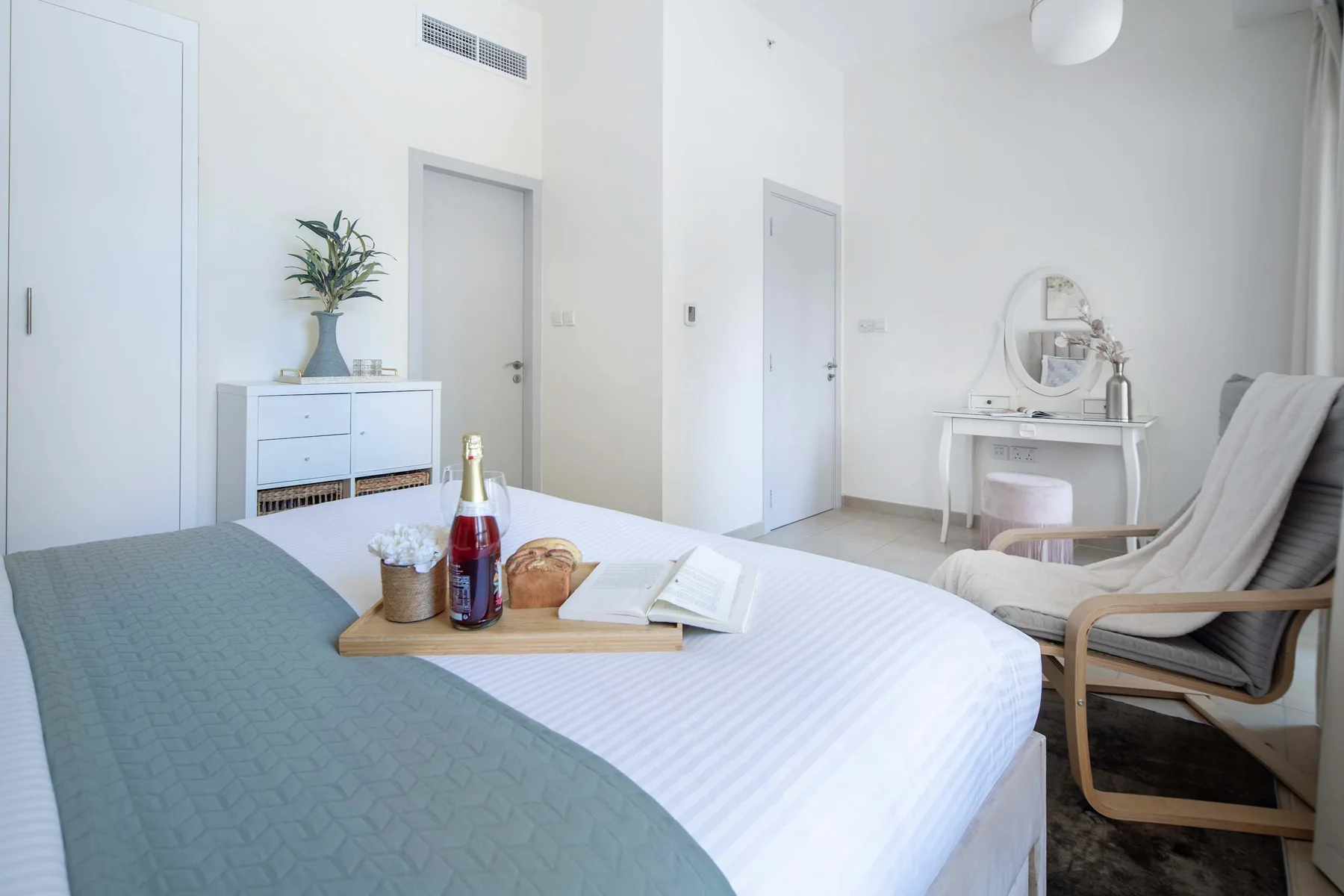 Un dormitorio luminoso con una cama bien hecha y un pequeño tocador.