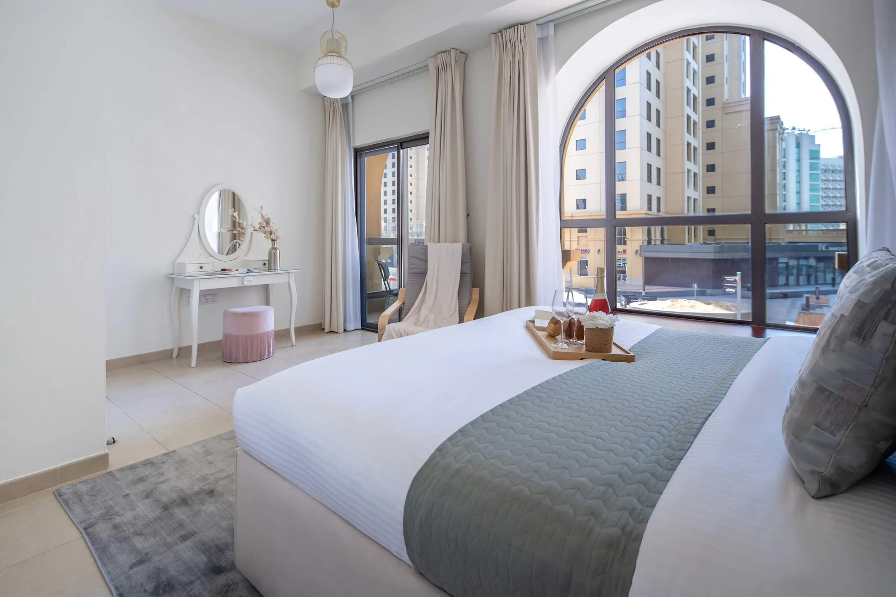 Un dormitorio luminoso con una gran ventana arqueada y una cama bien arreglada.