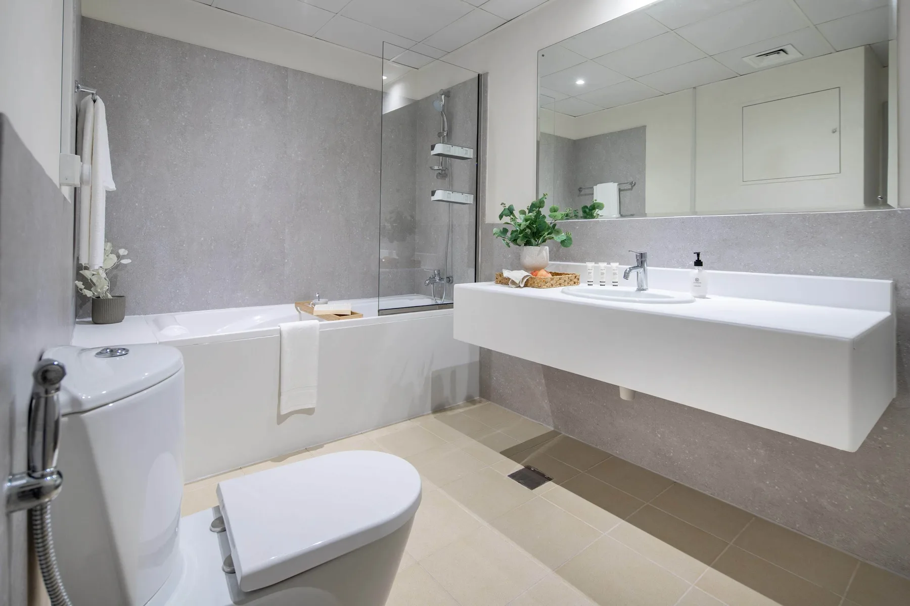 Un baño moderno con bañera, inodoro y un amplio lavabo bajo un espejo.
