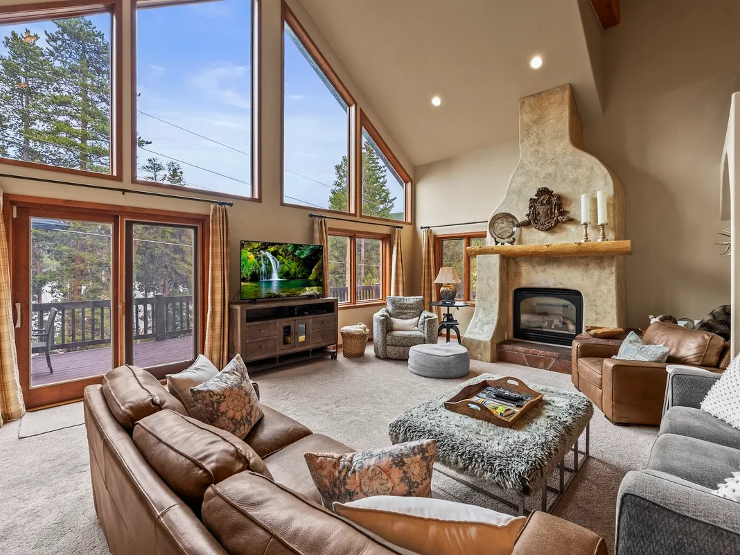 A spacious living room with tall windows, seating, and a stone fireplace.