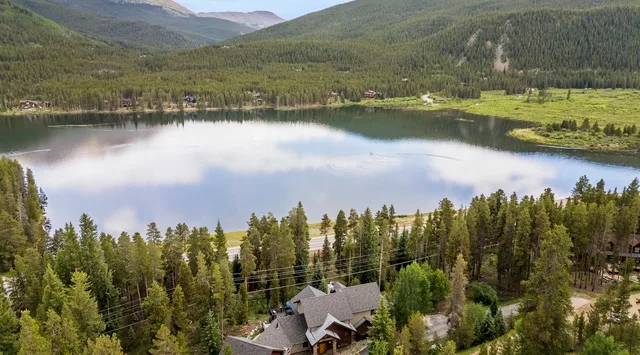 A lake lies among forested hills, with a house visible among trees in the foreground.