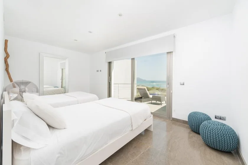 Un dormitorio luminoso con ropa de cama blanca y puertas corredizas de vidrio hacia un balcón.