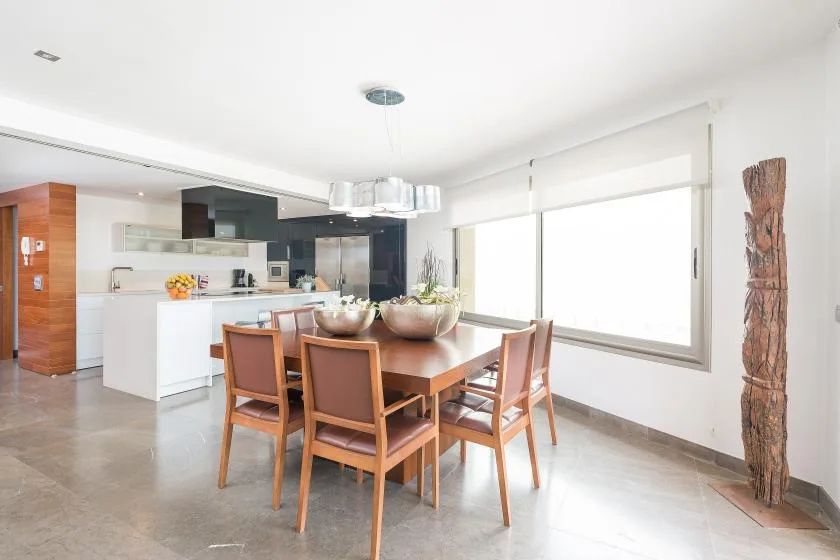 Un comedor luminoso con una mesa de madera junto a una cocina abierta.