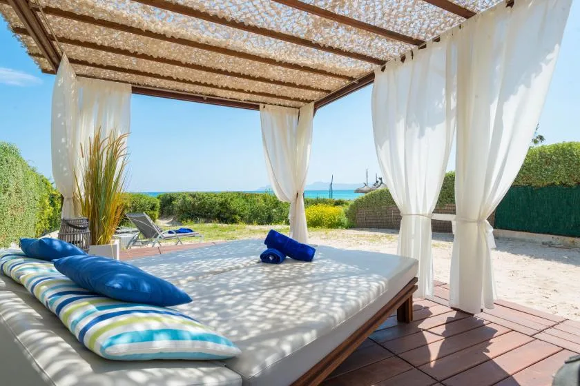 Una cama de día al aire libre está bajo una pérgola junto al mar.
