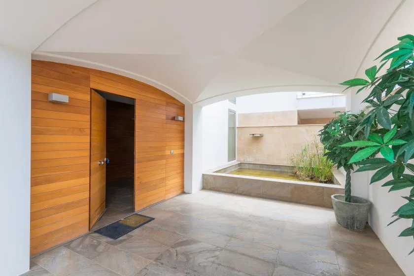 Un patio cubierto con una puerta de madera, piso de baldosas y plantas en macetas.