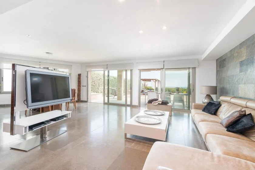 Una sala luminosa con televisor, asientos y grandes puertas de vidrio que dan a un balcón.