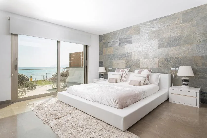 Un dormitorio luminoso con una cama blanca junto a grandes puertas corredizas de vidrio.