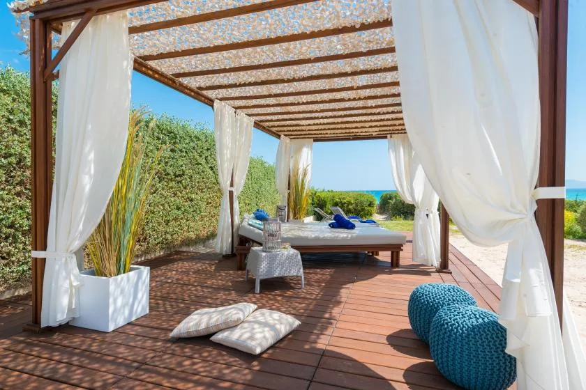 Una terraza exterior sombreada con cama de día y cortinas blancas da al mar.
