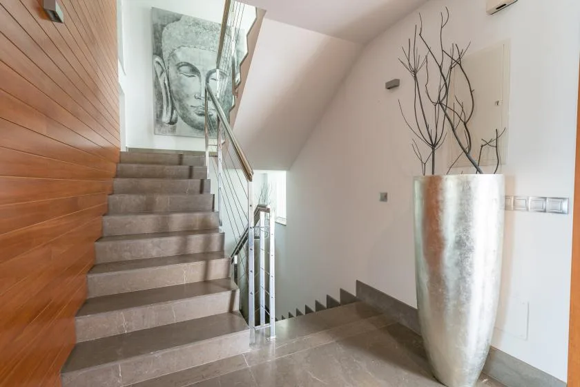 Una escalera interior con barandales metálicos, una maceta grande y un cuadro en la pared.