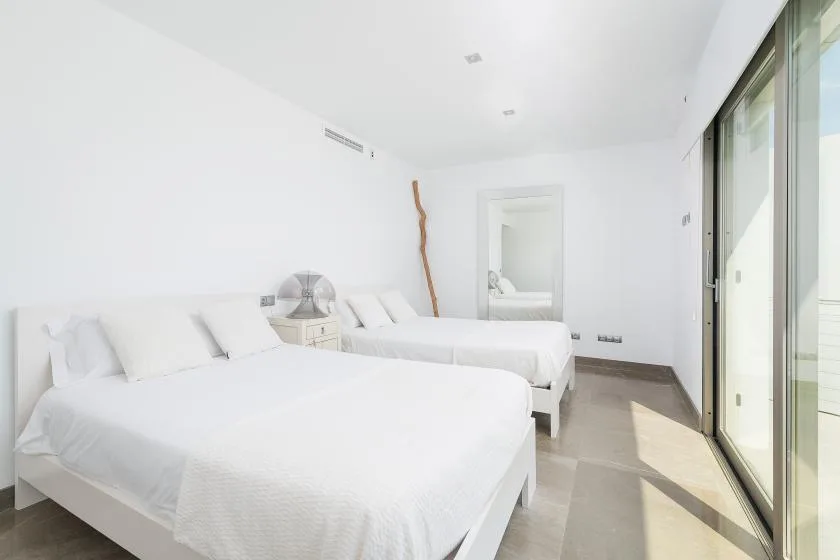 Un dormitorio luminoso con ropa de cama blanca y una gran puerta corrediza de vidrio.