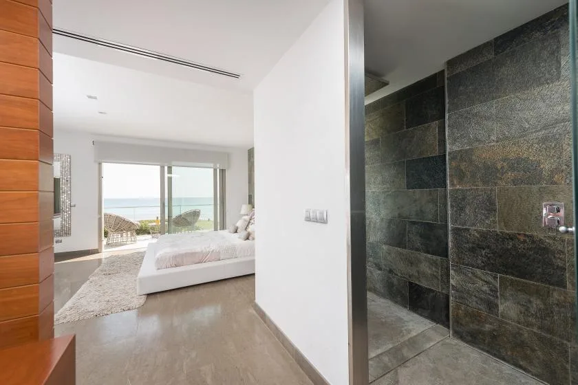 Un dormitorio luminoso con una ventana amplia junto a una ducha de azulejos oscuros.