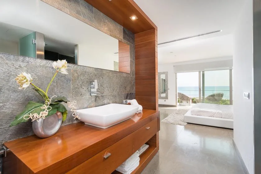 Un tocador de baño moderno da a un dormitorio con una gran ventana hacia el mar.
