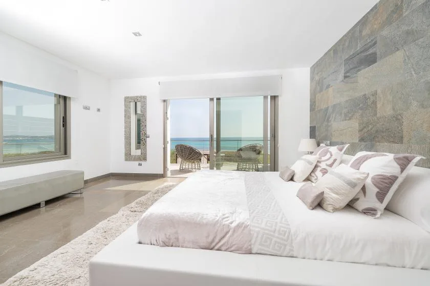 Un dormitorio luminoso con una cama grande frente a puertas de vidrio y vistas al mar.