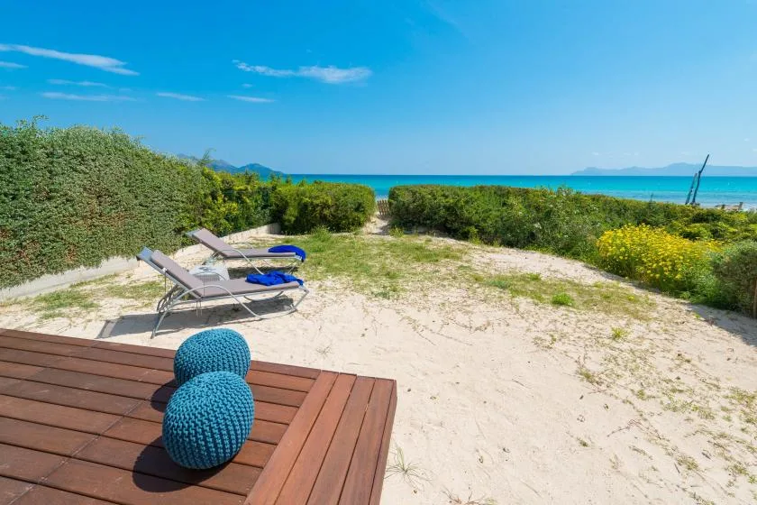 A sandy outdoor area beside the sea has lounge seating and a wooden deck.