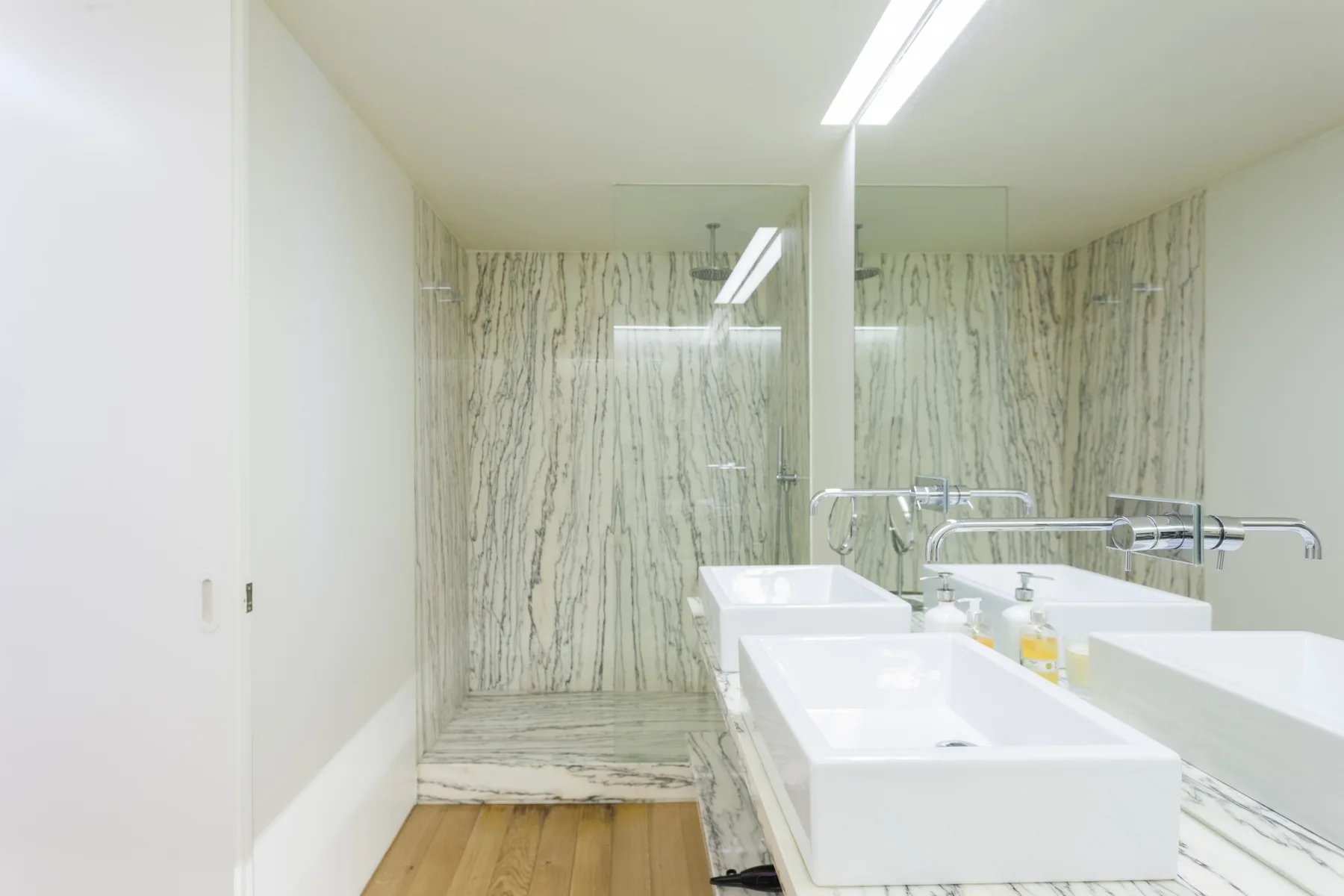 A bright bathroom with a glass shower, stone-patterned walls, and a long vanity.