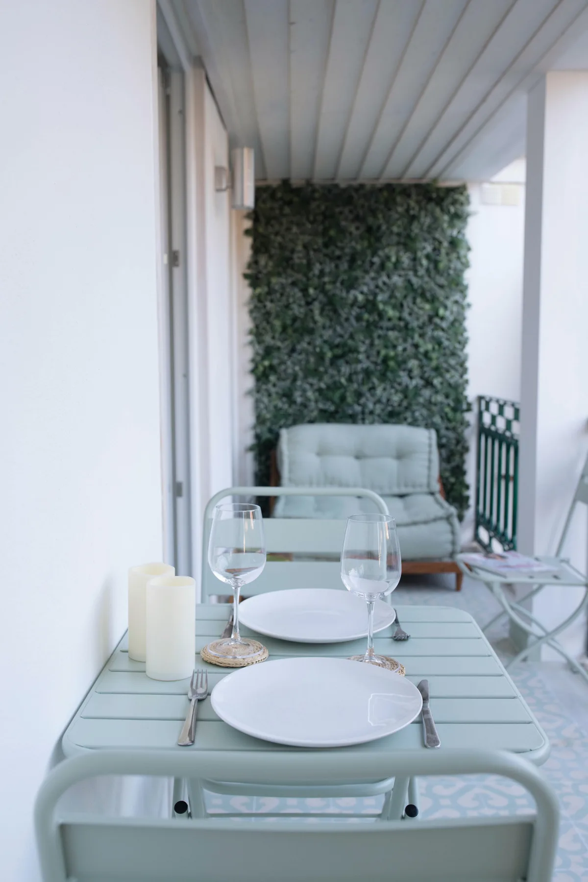 A covered terrace dining area with a set table and greenery along the back wall.