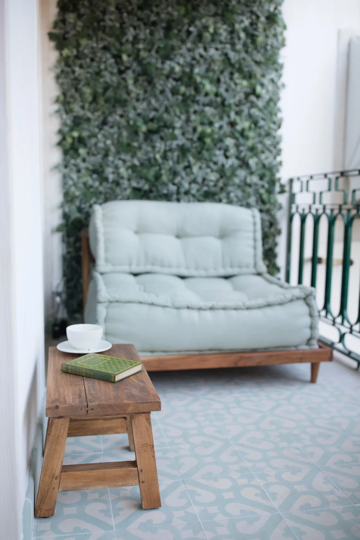 A small seating area with a pale cushioned seat, wooden table, and leafy wall.