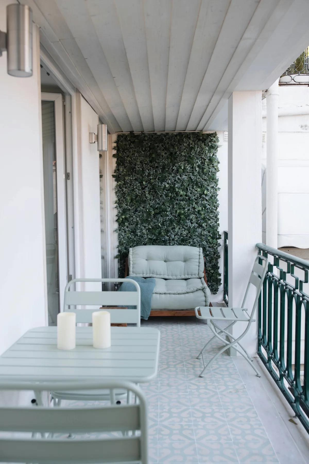 A covered terrace with pale outdoor seating and a leafy wall.