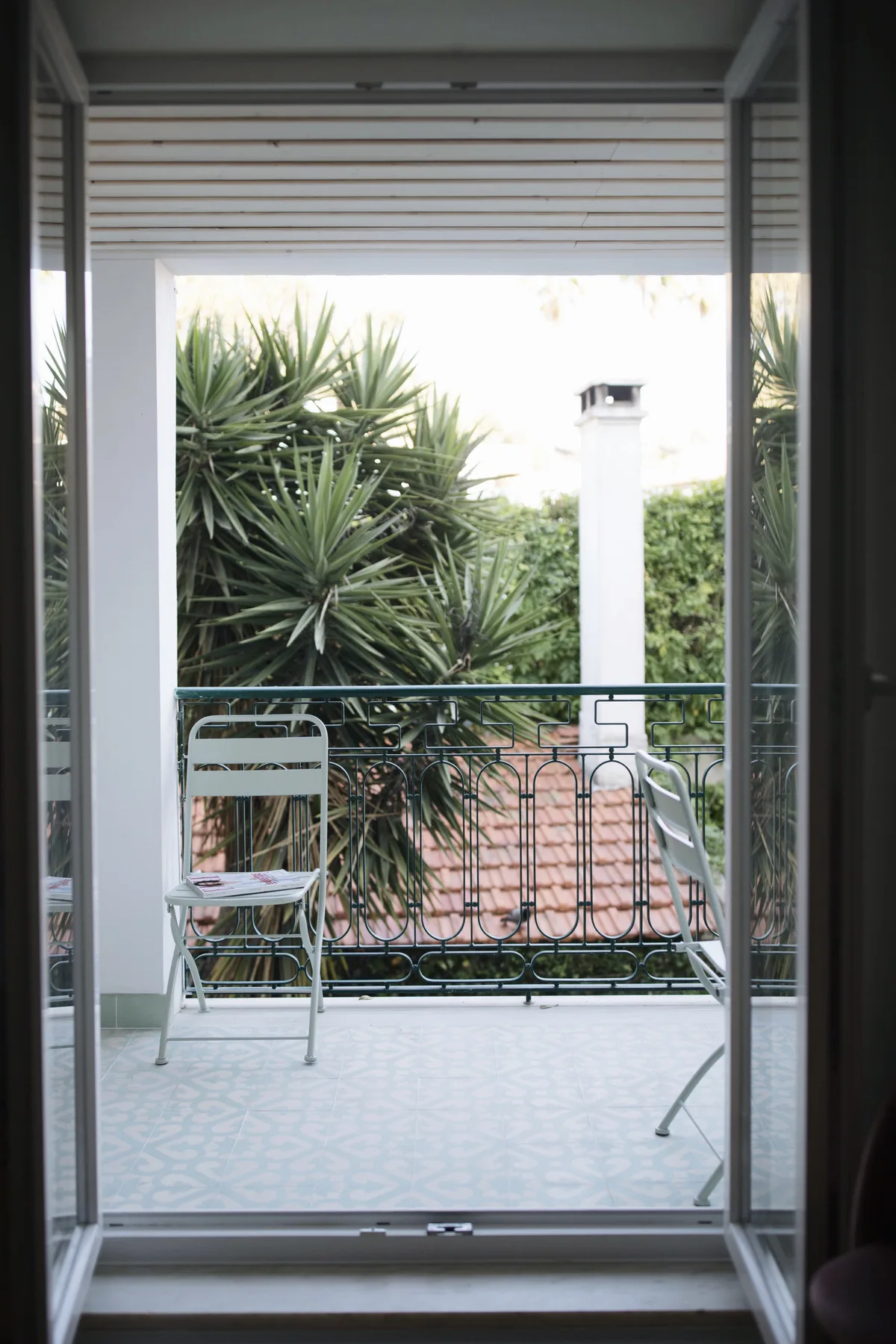 A tiled terrace with outdoor seating overlooks leafy greenery beyond a metal railing.