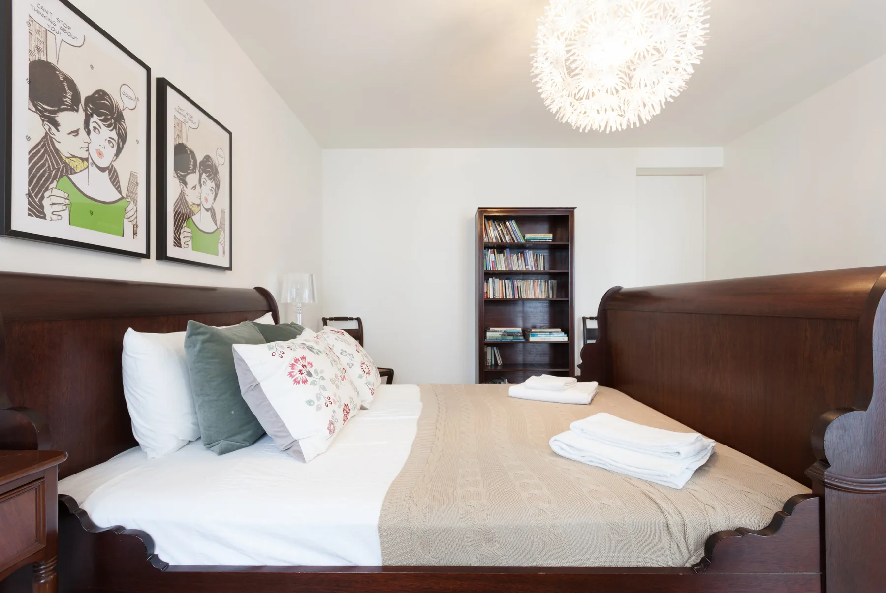 A bedroom with a neatly made bed and a bookcase against the back wall.
