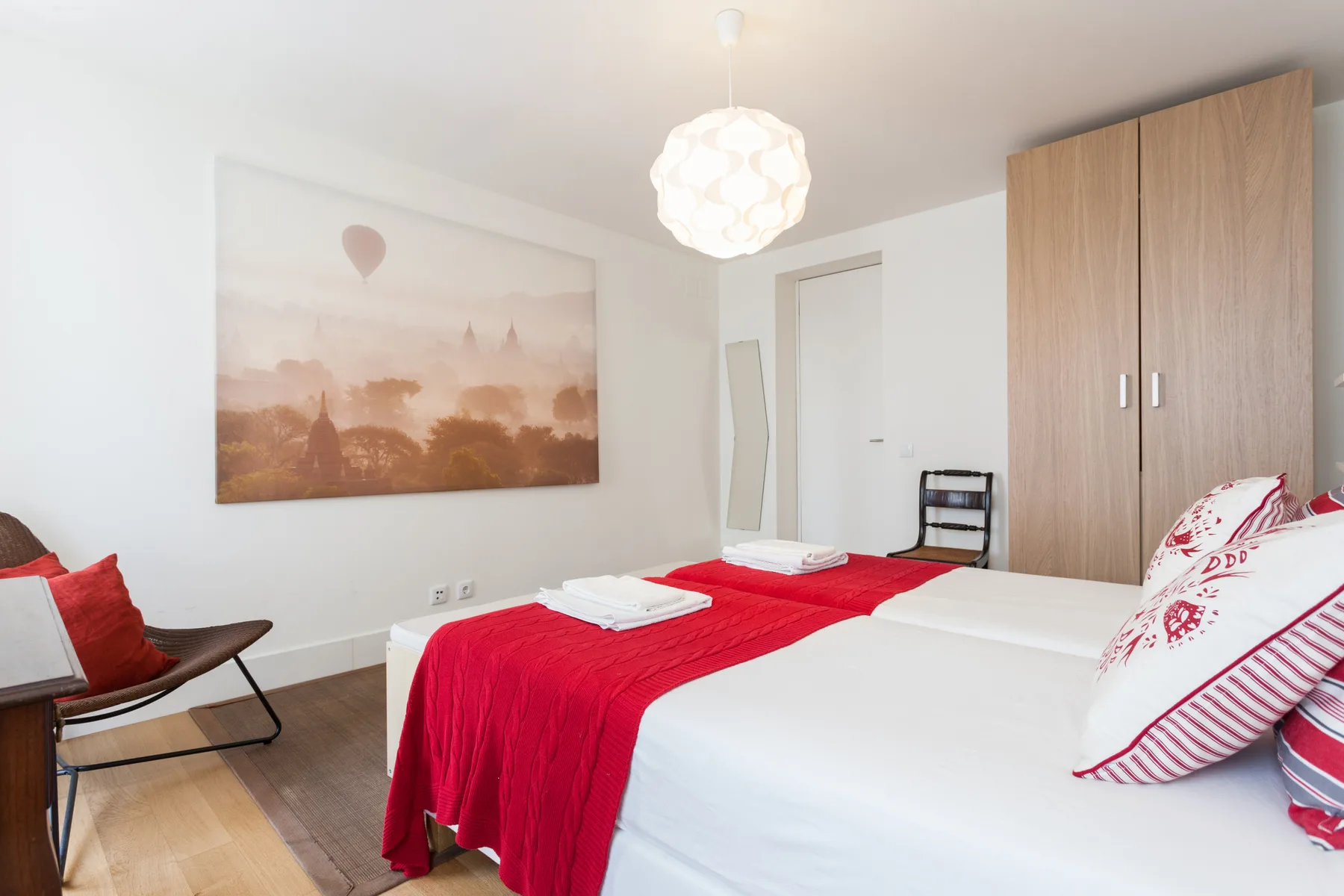A bedroom with two beds dressed in white and red linens.